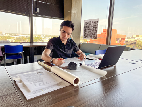 Conference room at One Riverwalk Place with a participant working at a table with documents, plans, and a laptop beside floor-to-ceiling windows.