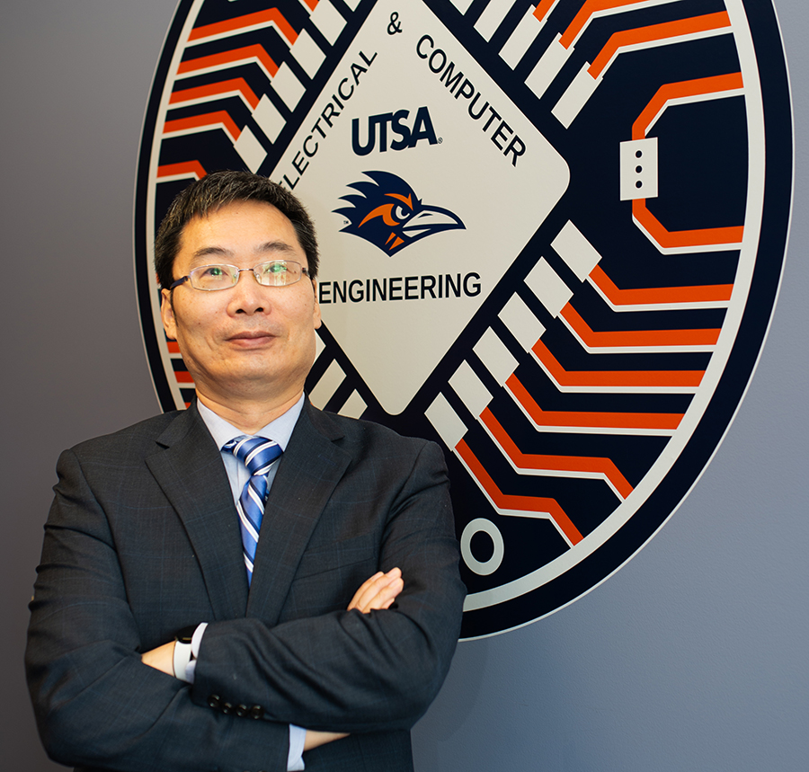 Dr. CJ Qian, wearing a suit with arms crossed, stands confidently in front of the UTSA Electrical and Computer Engineering emblem, reflecting his decade of leadership as department chair.