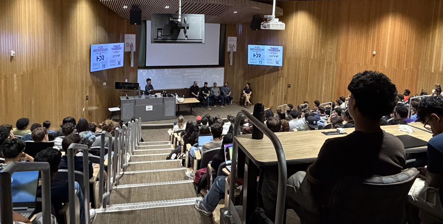 A large lecture hall filled with students listens to a panel discussion at the front of the room during the Klesse College first-year experience