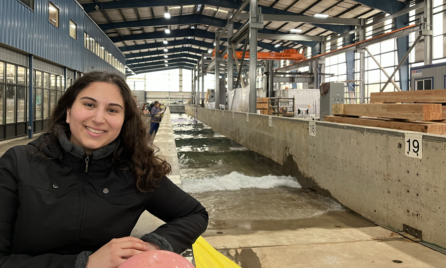 NHERI REU student poses next to a wave flume at the Oregon State University NHERI Wave Research Laboratory