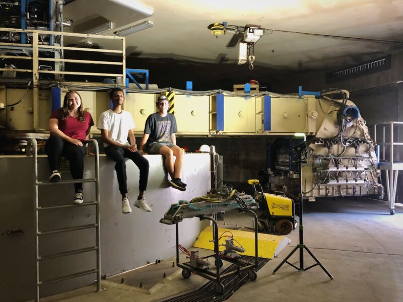 Three NHERI REU students sit on the support of the NHERI geotechnical centrifuge facility at the University of California, Davis