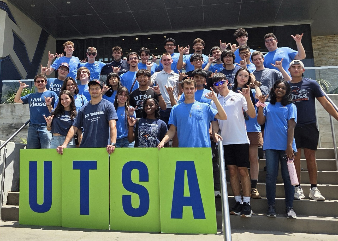 Participants of the Klesse College Summer Bridge Program gathered in an auditorium with a faculty member at the center, all smiling and pointing, showcasing the sense of community and connections built during the program. The diverse group reflects the supportive environment that continues throughout their freshman year.
