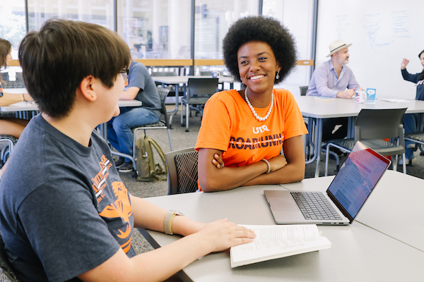Two students studying together at a table with a laptop in a tutoring center.